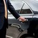 A driver wearing a suit with his hand on the door handle of a luxury sedan